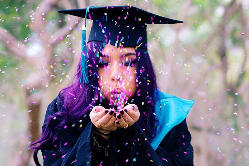 woman blows confetti at college graduation